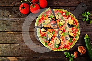 Healthy, gluten free green vegetable crust pizza with tomatoes, zucchini and mushrooms, table scene over dark wood