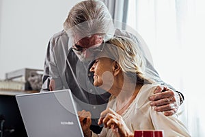 Healthy grandfather and grandmother using laptop for entertainment and shopping