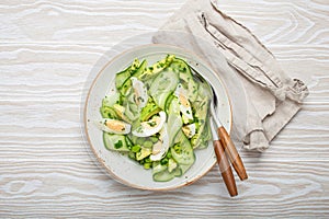 Healthy green avocado salad bowl with boiled eggs, sliced cucumbers, edamame beans, olive oil and herbs on ceramic plate