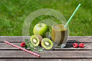 Healthy green smoothie in a glass with fresh fruits on a wooden table and natural background