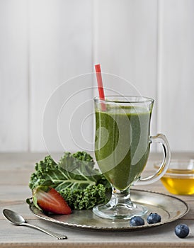 Healthy green smoothie with kale, strawberries, blueberries and honey in bottle with label on rustic wood background.