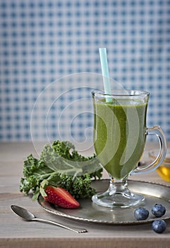 Healthy green smoothie with kale, strawberries, blueberries and honey in a glass against a rustic wood background.