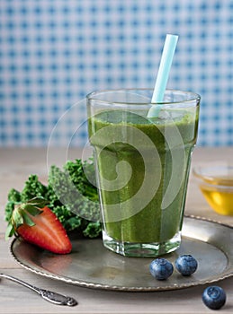 Healthy green smoothie with kale, strawberries, blueberries and honey on a vintage plate in a glass against a rustic wood backgrou