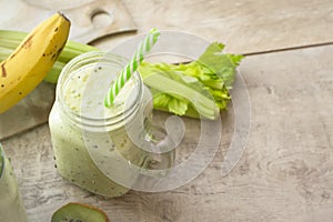 Healthy green smoothie made from celery, spinach, kiwi, bananas in a glass jar on a wooden rustic table, copy space