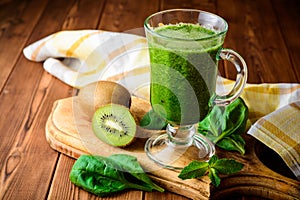 Healthy green smoothie with spinach and kiwi in glass on rustic wooden background.