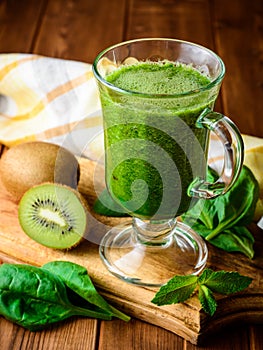 Healthy green smoothie with spinach and kiwi in glass on rustic wooden background.