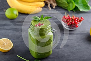 Healthy green spinach smoothie in a jar mug decorated with mint and red currant berries with ingridients on the black wooden table