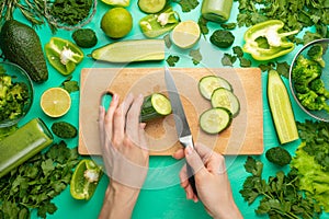 Healthy green vegan cooking ingredients. Flay-lay of female hands cutting green vegetables and greens over a wooden board, top