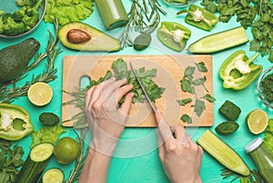 Healthy green vegan cooking ingredients. Flay-lay of female hands cutting green vegetables and greens over a wooden board, top