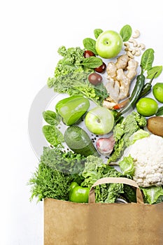 Healthy green vegan vegetarian food in full paper bag, vegetables and fruits on white background. Shopping food supermarket, raw