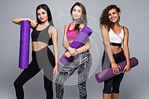 Healthy group of three people doing gym and standing and holding colorful mats isolated on white background