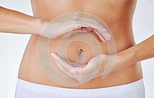 A healthy gut comes from unified bacteria. a woman cupping her hands above her belly against a studio background.