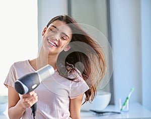 With healthy hair you can face your day with confidence. a beautiful young woman blowdrying her hair in the bathroom at