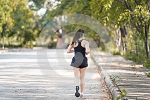 A healthy happy Asian woman runner in black sport outfits jogging in the natural city park under evening sunset