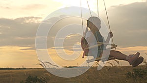 Healthy happy child rides on a rope swing on branch in park. little cheerful girl laughs, rejoices and waves her arms in