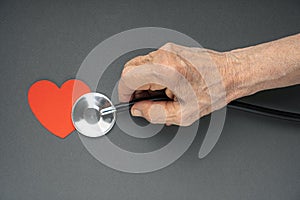 Healthy heart in old age concept. Elderly hands with stethoscope listen the heart shape