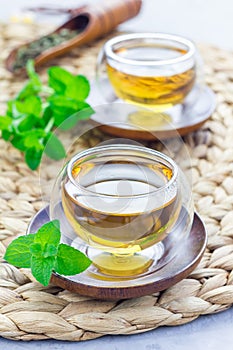 Healthy herbal mint tea in oriental glass cup with fresh peppermint and tea scoop on background