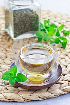 Healthy herbal mint tea in oriental glass cup with fresh peppermint and tea scoop on background