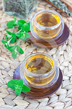 Healthy herbal mint tea in oriental glass cup with fresh peppermint and tea scoop on background