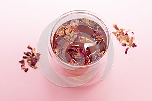 Healthy herbal rose petals, buds tea in double walled glass cup on pink background