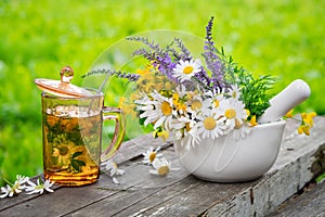 Healthy herbal tea cup, mortar of medicinal herbs on wooden board.