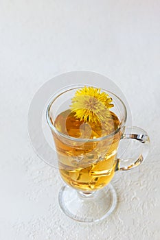 Healthy herbal tea with dandelions in a glass cup, ice and yellow dandelion flower inside on a white background