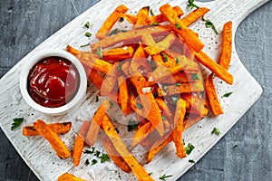 Healthy Homemade Baked Orange Sweet Potato Fries with ketchup, salt, pepper on white wooden board