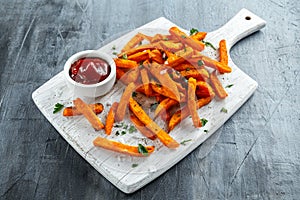 Healthy Homemade Baked Orange Sweet Potato Fries with ketchup, salt, pepper on white wooden board