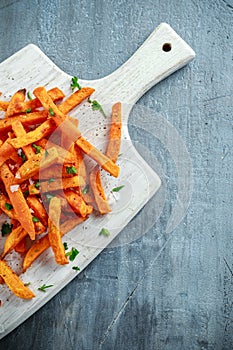 Healthy Homemade Baked Orange Sweet Potato Fries with ketchup, salt, pepper on white wooden board