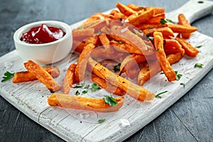 Healthy Homemade Baked Orange Sweet Potato Fries with ketchup, salt, pepper on white wooden board