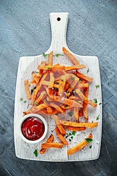 Healthy Homemade Baked Orange Sweet Potato Fries with ketchup, salt, pepper on white wooden board