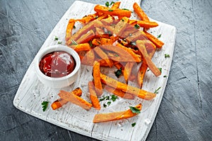 Healthy Homemade Baked Orange Sweet Potato Fries with ketchup, salt, pepper on white wooden board