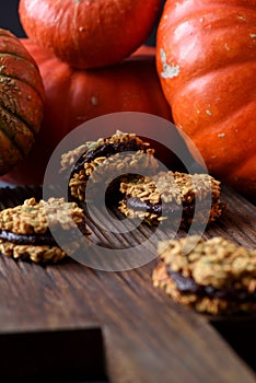 Healthy homemade dessert. Pumpkin oatmeal breakfast cookie sandwiches with chocolate and winter squashes on oak board