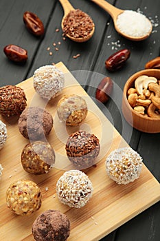 Healthy homemade energy balls with cranberries, nuts, dates and rolled oats on cutting board on black background. Vertical photo