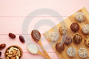 Healthy homemade energy balls with cranberries, nuts, dates and rolled oats on cutting board on pink background. Space for text