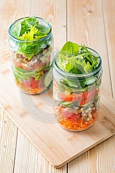 Healthy homemade mason jar salad with fresh pear tomatoes, carrots and herbs. Vegetarian concept