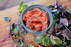 Healthy homemade tomato and red hot chili pepper sauce in a black bowl, and fresh basil on wooden board on table.