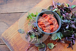 Healthy homemade tomato and red hot chili pepper sauce in a black bowl, and fresh basil on wooden board on table.