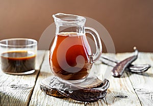 Healthy immune carob molasses beverage in glass jar, carob pods, molasses in glass, wooden and brown background