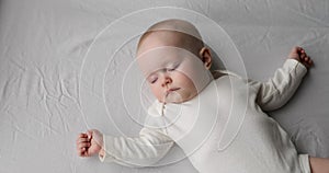 Healthy infant sleep alone on big bed spreading hands wide