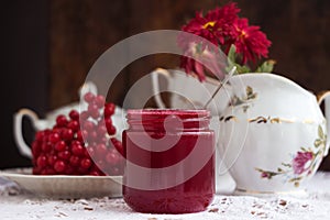 Healthy jam from viburnum berries Viburnum opulus in a glass jar, a bunch of viburnum, antique dishes and chrysanthemums in a