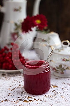 Healthy jam from viburnum berries Viburnum opulus in a glass jar, a bunch of viburnum, antique dishes and chrysanthemums