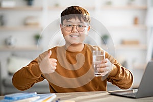 Healthy japanese teenager holding glass of water while studying