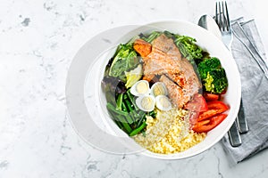 Healthy keto food concept. Fish salad bowl on marble background. Salad with salmon, couscous, vegetables, quail eggs