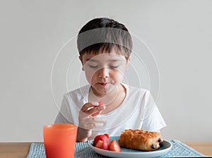 Healthy kid eating strawberry and chocolate croissant, Portrait boy having breakfast, Child eating healhty food at home