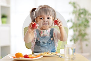 Healthy kids nutrition concept. Cheerful toddler girl sitting at table with plate of salad, vegetables, pasta in room photo