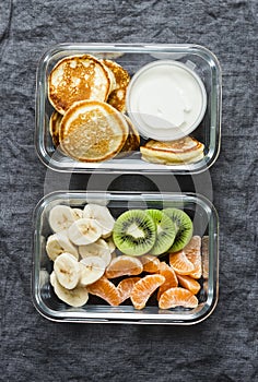 Healthy kids school, walk, picnic lunch box - pancakes with sour cream and banana, kiwi, tangerine fruit. Delicious snack