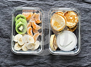 Healthy kids school, walk picnic lunch box - pancakes with sour cream and banana, kiwi, tangerine fruit. Delicious snack on a
