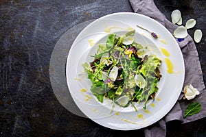 Healthy lettuce arugula salad with edible flowers and microgreens on white plate, dark background. Top view