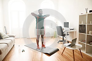 Healthy life. Full length shot of male fitness instructor showing exercises with resistance band while streaming